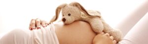 Schwangere Frau mit einem Kuscheltier auf Ihrem Bauch